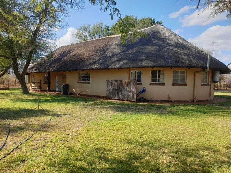 Rear view of a traditional farmhouse featuring a thatched roof, plastered exterior walls, and established garden surroundings.