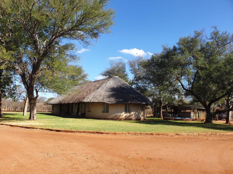 A traditional farm-style dwelling featuring a classic thatched roof and plastered exterior walls, set within a spacious, well-maintained garden landscape.