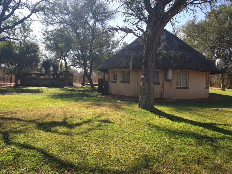 A view of a traditional thatched-roof farm cottage set within a spacious, tree-lined garden area.