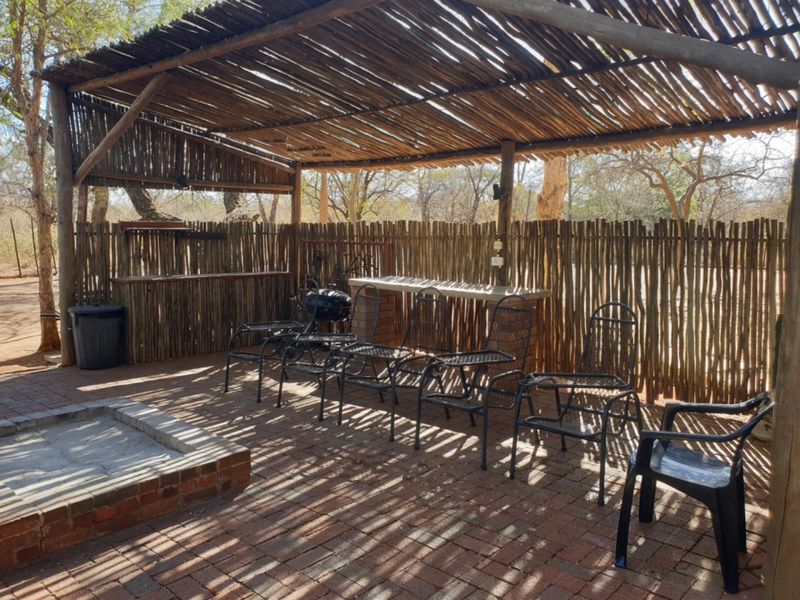 Outdoor entertainment area featuring a thatched roof, brick fire pit, and built-in bar counter, set within a rustic timber-fenced patio space.