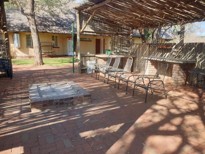 Outdoor entertainment area featuring a thatched pergola, built-in brick braai, and a central brick fire pit on a paved patio.