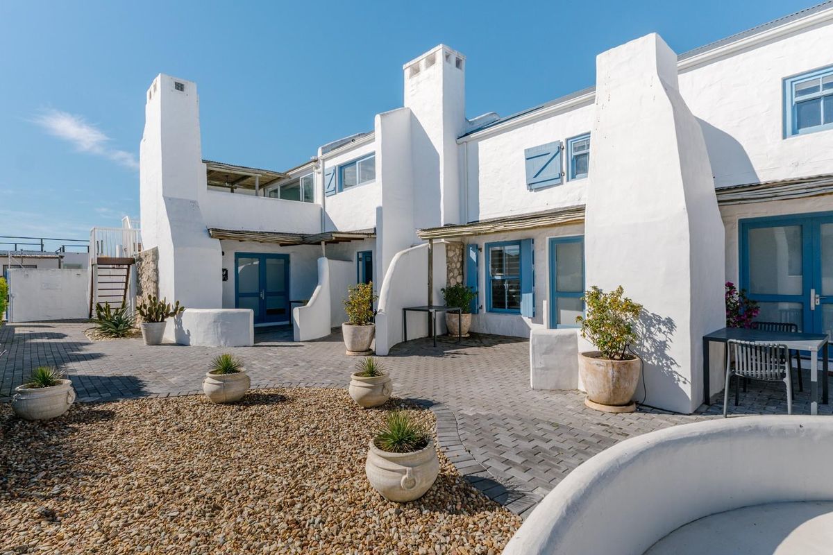 A well-maintained rear courtyard featuring paved areas, gravel landscaping, and distinctive white architectural facades with blue shutters and external chimneys.
