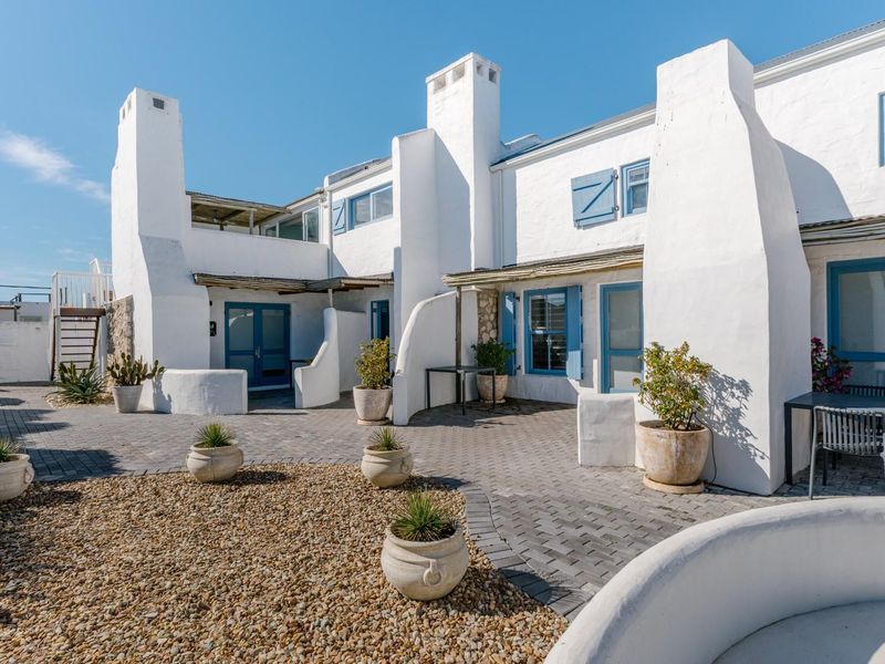 A well-maintained rear courtyard featuring paved areas, gravel landscaping, and distinctive white architectural facades with blue shutters and external chimneys.