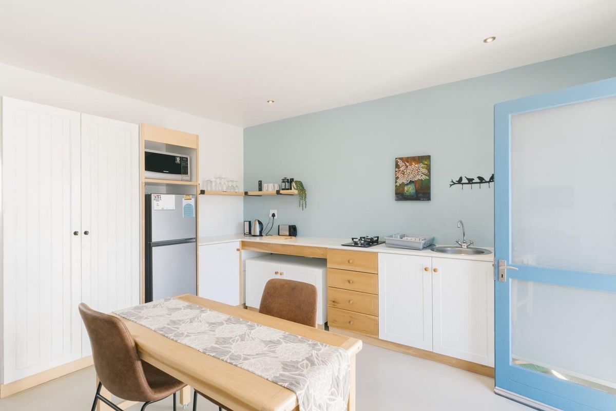 A bright, modern kitchen featuring white cabinetry, timber accents, a built-in cooktop, and a sink, complemented by a soft blue feature wall.
