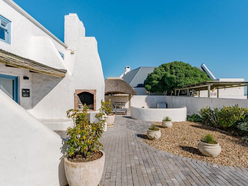 A well-maintained rear courtyard featuring a paved walkway, gravel garden, built-in braai, and a charming thatched gazebo area.