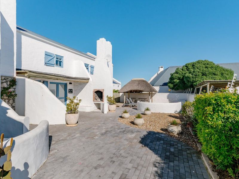 A well-maintained rear courtyard featuring a paved patio, built-in braai, and a charming thatched lapa, perfect for outdoor entertaining.