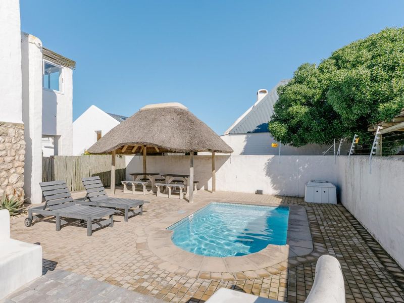 Outdoor pool area featuring a paved patio, a thatched lapa for shade, and secure boundary walls with electric fencing.