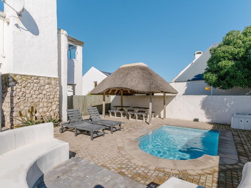 Outdoor pool area featuring a paved patio, built-in seating, and a traditional thatched lapa, perfect for relaxation and entertaining.