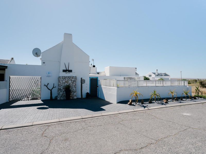 Front elevation of a white-painted house featuring a paved driveway, stone-clad chimney detail, and secure gated entrance.