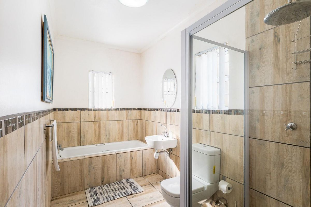A well-maintained bathroom featuring a built-in bathtub, wall-mounted basin, toilet, and a separate glass-enclosed shower with wood-look ceramic tiling.
