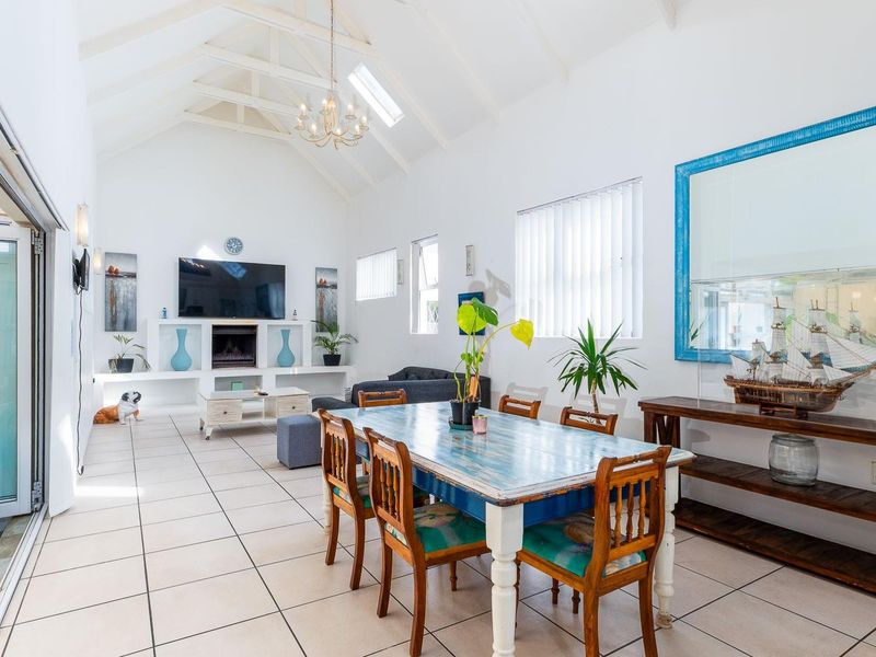 Spacious open-plan living and dining area featuring a high vaulted ceiling, skylights, tiled flooring, and a built-in fireplace with seamless access to the patio.