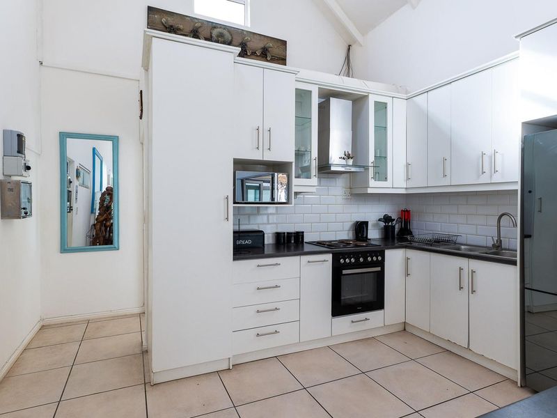 A bright, functional kitchen featuring white cabinetry, subway tile backsplash, built-in oven, hob, extractor fan, and tiled flooring under a vaulted ceiling.