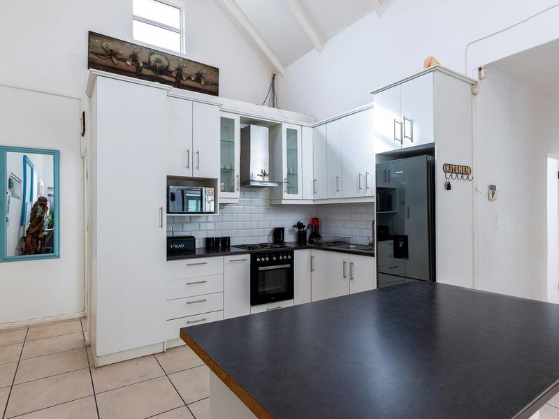 A bright kitchen featuring white cabinetry, a subway tile backsplash, built-in oven and hob, and a central island under a high vaulted ceiling.