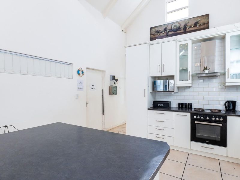 A bright kitchen featuring white cabinetry, subway tile backsplash, built-in appliances, and a high vaulted ceiling with tiled flooring.