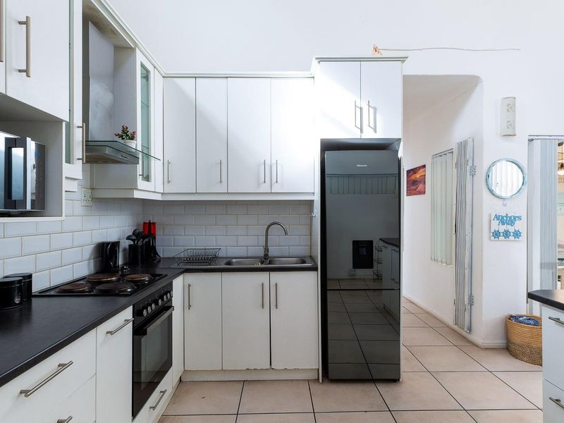 A functional kitchen featuring white cabinetry, subway tile backsplash, dark laminate countertops, and integrated appliances with tiled flooring.