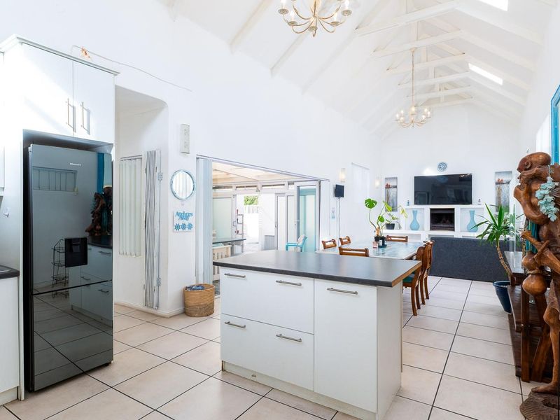 Spacious open-plan living area featuring a modern kitchen with island, vaulted ceilings with exposed rafters, tiled floors, and a cozy built-in fireplace.