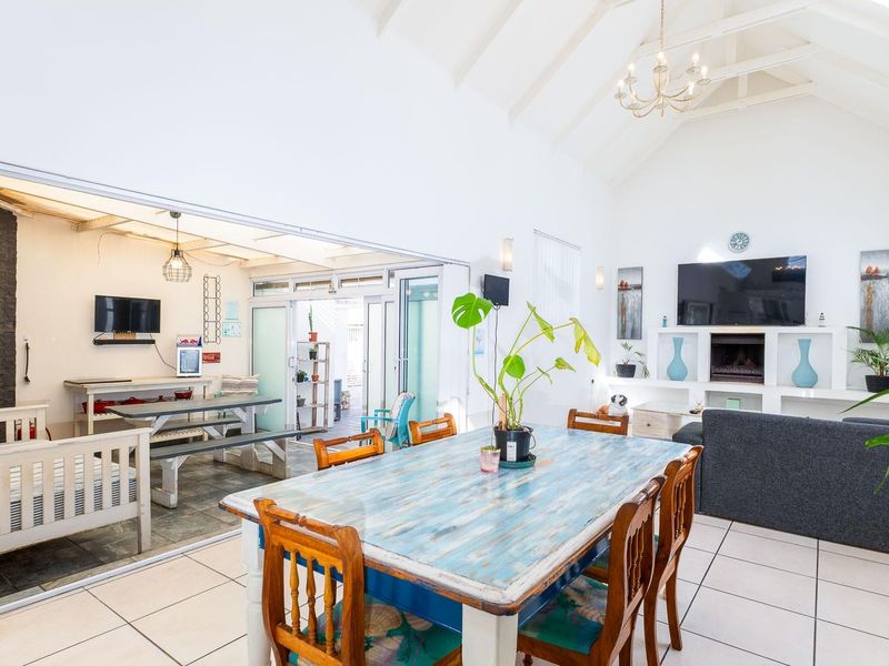 Spacious open-plan living and dining area featuring a vaulted ceiling with exposed rafters, tiled flooring, and seamless flow to an outdoor patio space.