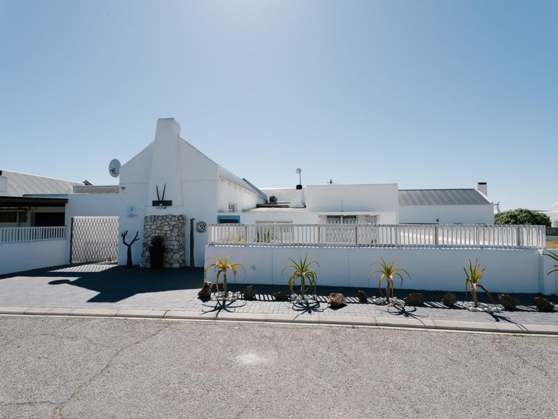 Front elevation of a white-painted house featuring a paved driveway, stone-clad chimney detail, and a secure boundary wall with gated access.