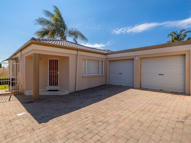Front view of a well-maintained house featuring a double garage, paved driveway, and a secure entrance with a covered porch area.