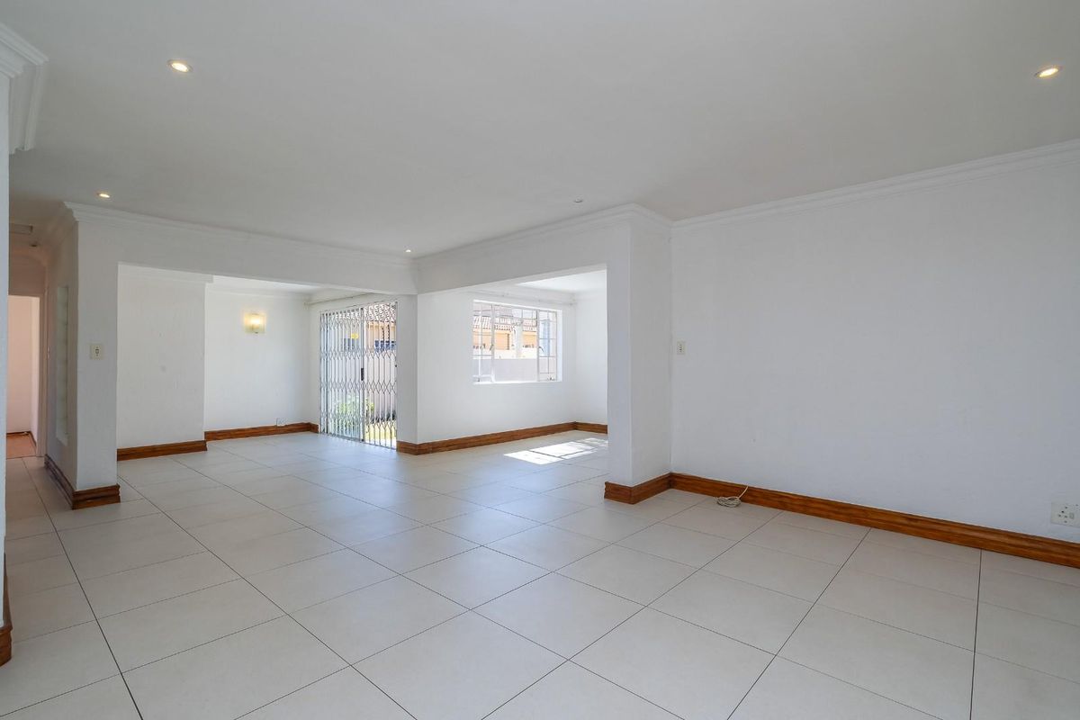 A spacious, open-plan living area featuring neutral tiled flooring, recessed downlighting, and clean white walls, providing a versatile blank canvas for interior design.