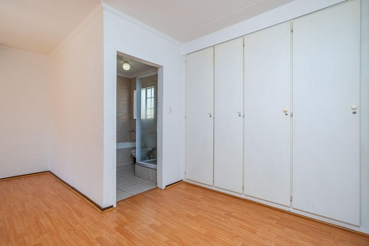 A bright, empty bedroom featuring laminate flooring, ample built-in cupboard space, and direct access to an en-suite bathroom.