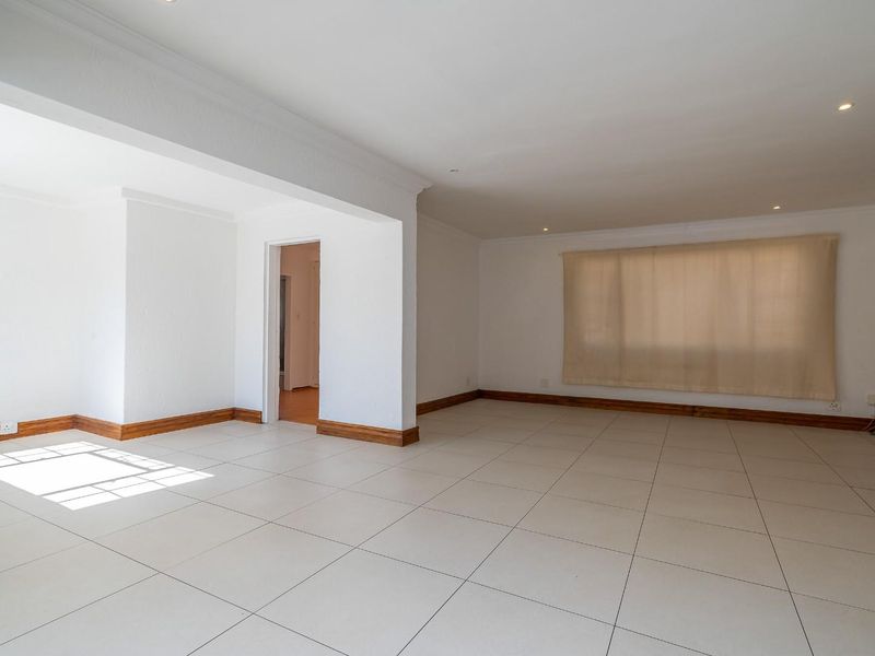 A spacious, bright, and empty living area featuring neutral tiled flooring, recessed lighting, and classic timber skirting boards, offering a versatile blank canvas.