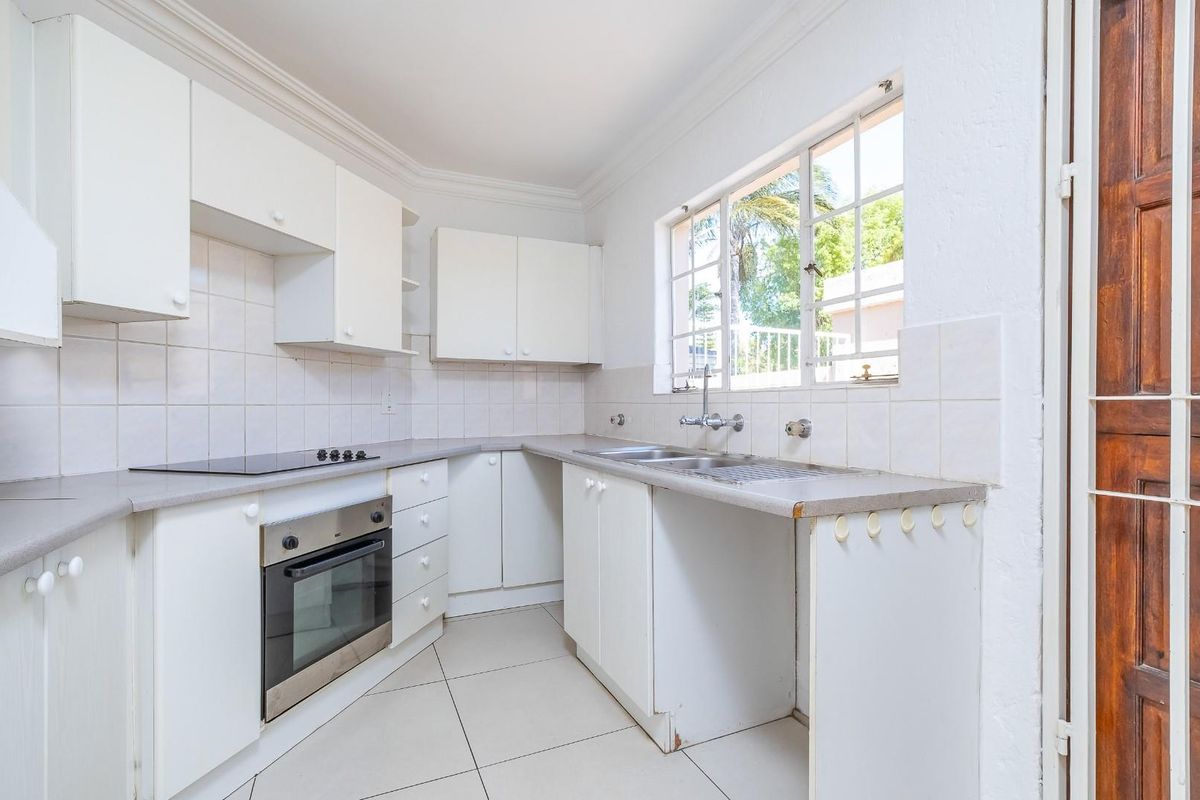 A functional kitchen featuring white built-in cabinetry, a tiled backsplash, electric hob, built-in oven, and a double sink with natural light.