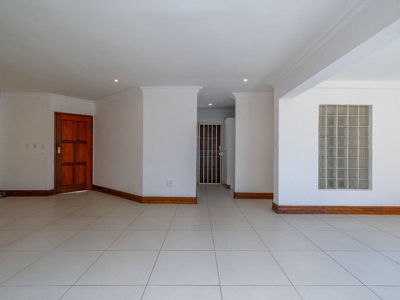 A spacious, empty living area featuring neutral tiled flooring, a decorative glass block wall, and clean white finishes throughout.