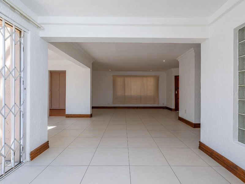 Spacious, open-plan living area featuring neutral tiled flooring, a decorative glass block window, and a secure sliding door entrance.