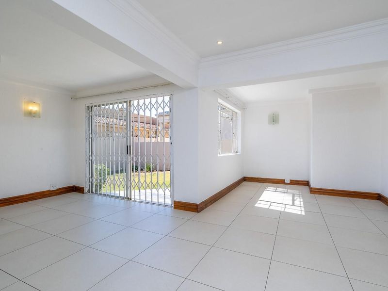 A bright, open-plan living area featuring neutral tiled flooring, timber skirting boards, and a sliding glass door with a security gate leading outdoors.