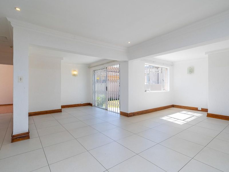 A bright, open-plan living area featuring neutral tiled flooring, recessed lighting, and a sliding door with security gate leading to the exterior.