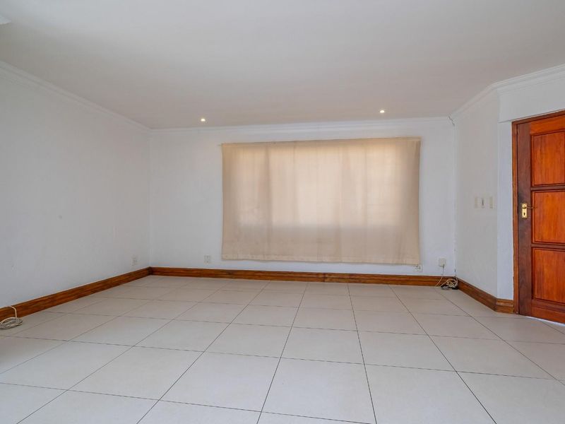 A bright, empty living room featuring neutral tiled flooring, wooden skirting boards, and a classic wooden door, ready for personalization.