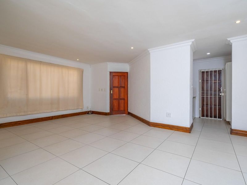 A spacious, empty living area featuring neutral tiled flooring, wooden skirting boards, and recessed downlighting, providing a clean canvas for interior design.