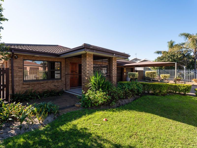 A well-maintained face brick house featuring a tiled roof, paved entrance, and a convenient carport, set within a neat garden with established landscaping.