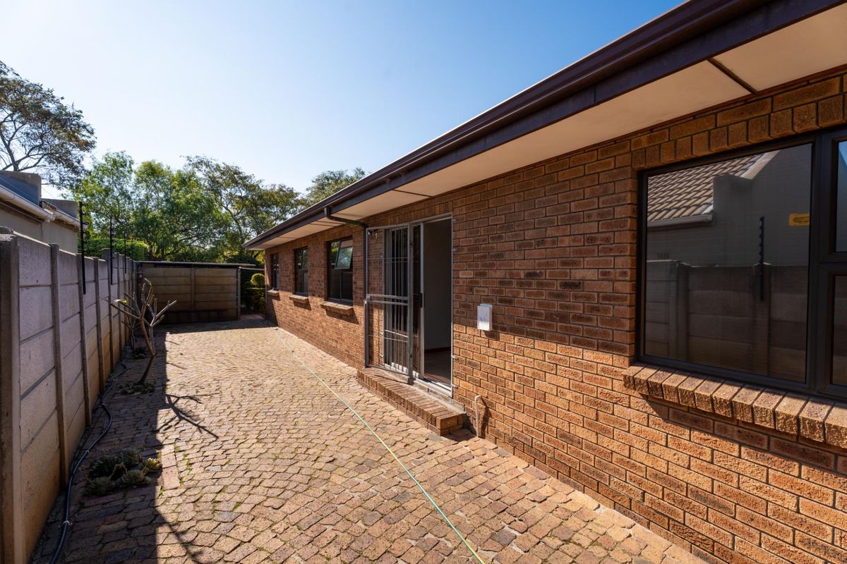 A view of the rear exterior featuring a face brick facade, paved patio area, and secure boundary walling.
