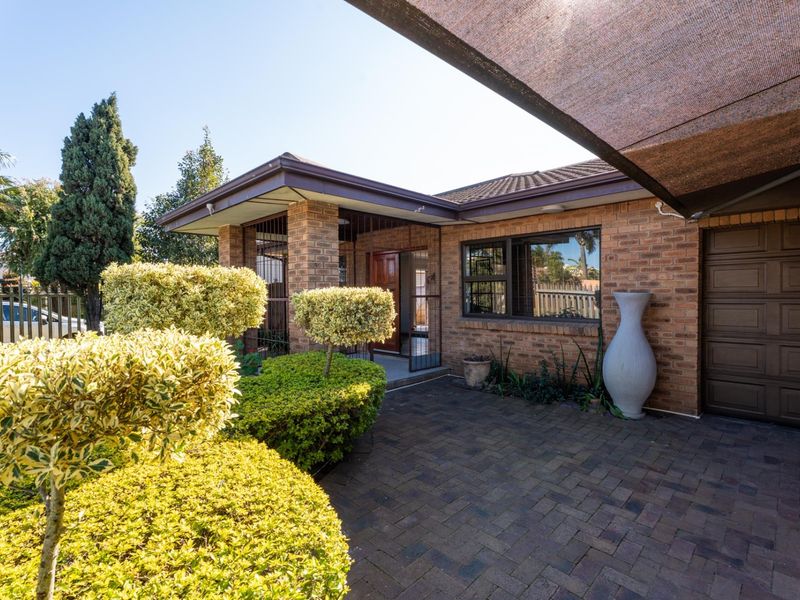 Front exterior view of a brick house featuring a paved driveway, garage access, and a covered entrance area with established garden landscaping.