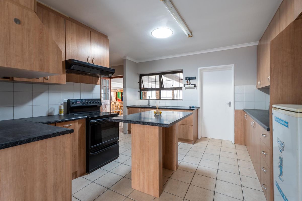 Functional kitchen featuring laminate cabinetry, dark countertops, a central island, and tiled flooring, offering a practical layout with potential for modern updates.