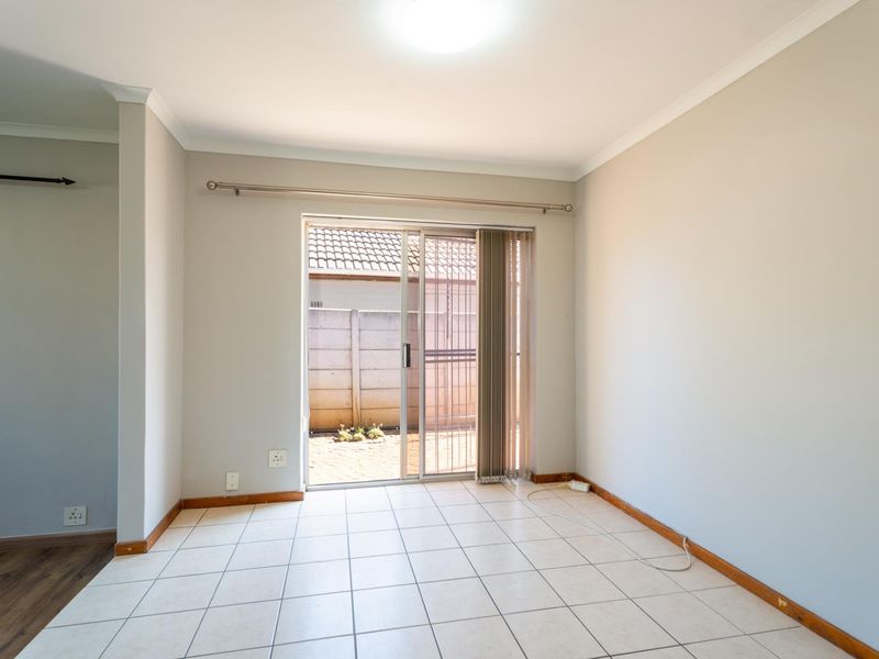 An empty living room featuring ceramic tile flooring, neutral walls, and a sliding glass door providing direct access to the rear exterior area.