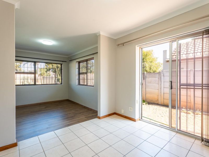 Bright, empty living area featuring a mix of laminate and tiled flooring with direct access to the rear garden through sliding glass doors.