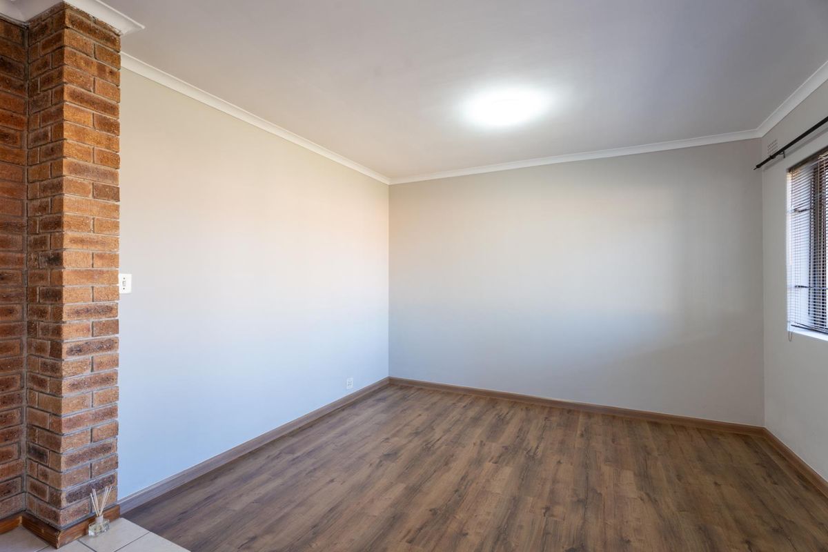 A bright, empty bedroom featuring laminate flooring, a distinctive exposed brick pillar, and neutral wall finishes, ready for personalization.