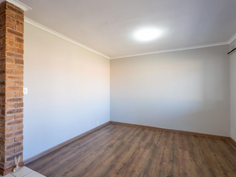 A bright, empty bedroom featuring laminate flooring, a distinctive exposed brick pillar, and neutral wall finishes, ready for personalization.