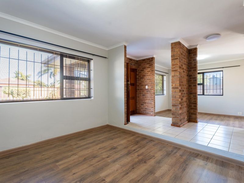 Spacious open-plan living area featuring a combination of laminate and tiled flooring, accented by distinctive exposed brick columns and large windows with security bars.