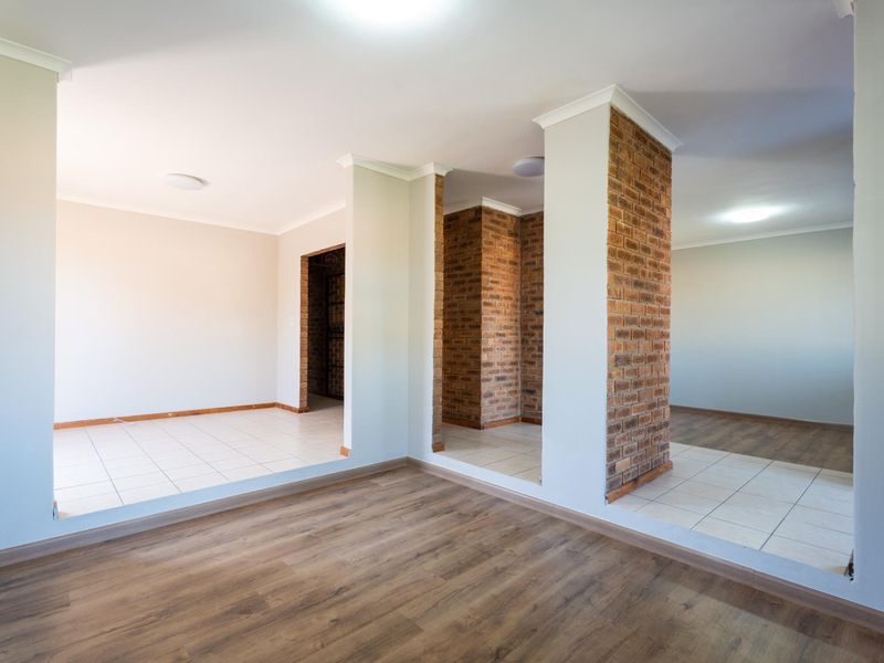 Spacious open-plan living area featuring exposed brick columns, a mix of laminate and tiled flooring, and neutral wall finishes.