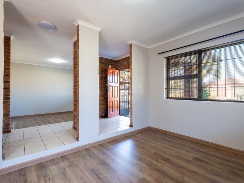 Bright living area featuring exposed brick pillars, a mix of laminate and tiled flooring, and large windows with fitted venetian blinds.