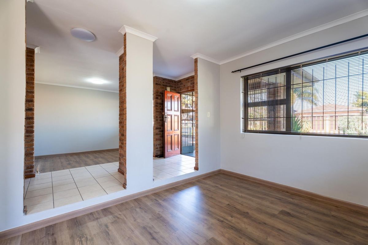 Bright living area featuring exposed brick pillars, a mix of laminate and tiled flooring, and large windows with fitted venetian blinds.