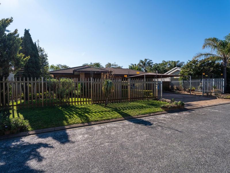 Front view of a single-story brick house featuring a paved driveway, carport, and secure perimeter fencing with integrated electric security wires.