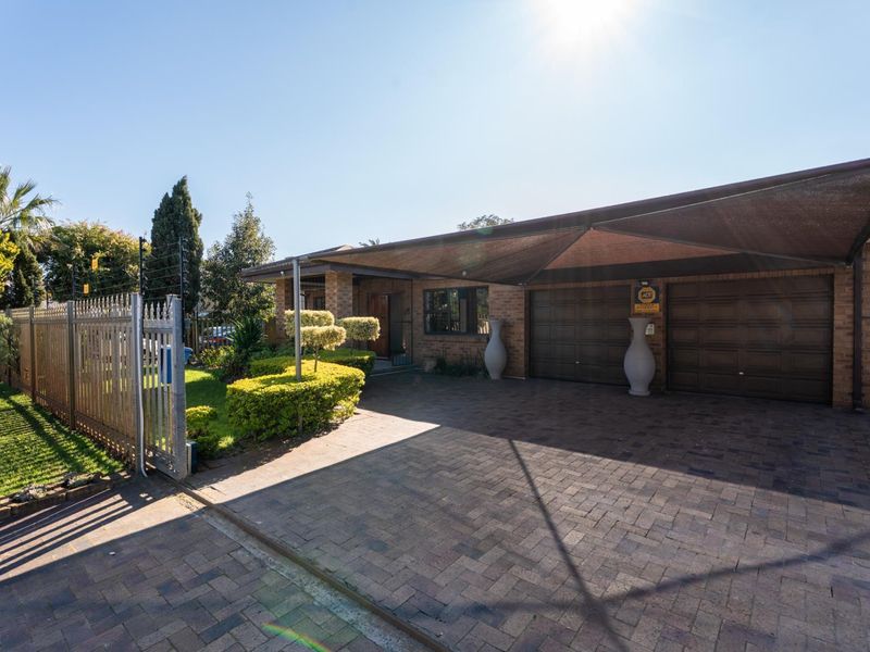 Front view of a brick house featuring a paved driveway, double garage with a shade cloth carport, and secure perimeter fencing.