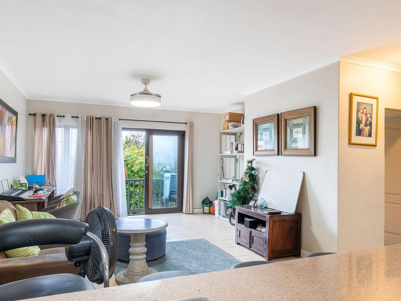 Open plan living area featuring tiled flooring, coved cornicing, and a sliding glass door providing access to an outdoor balcony space.