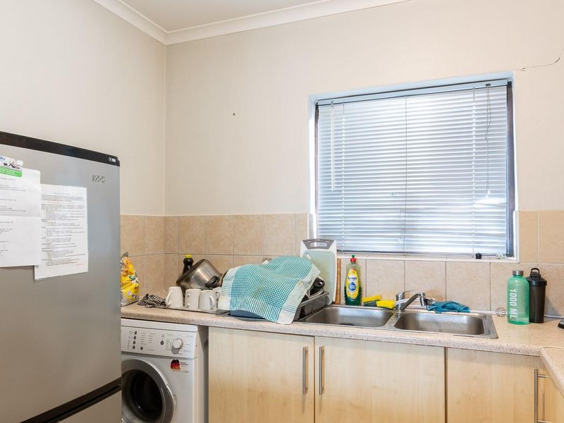 A functional kitchen area featuring laminate countertops, a double stainless steel sink, tiled splashbacks, and built-in cabinetry with an integrated washing machine space.