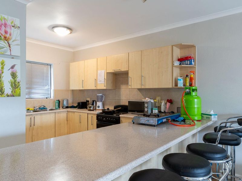 Functional kitchen featuring light wood-finish cabinetry, a breakfast bar counter, tiled backsplash, and a freestanding stove with integrated sink area.